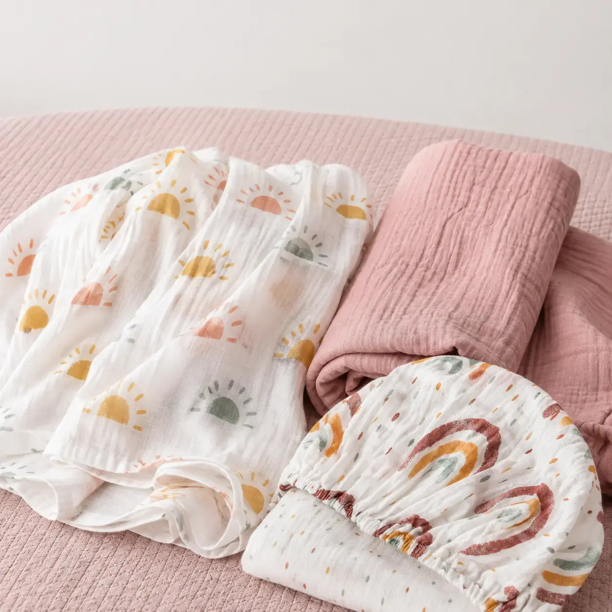 Peony Haze muslin swaddle and Sunbeam fitted cot sheet flat lay with minimalist sun print, birds eye view - Honey & Sage