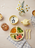 Children's meal set with plate, bowls, and utensils on a wooden table.