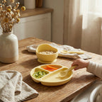 Yellow children's plate with compartments on a wooden table, filled with food.