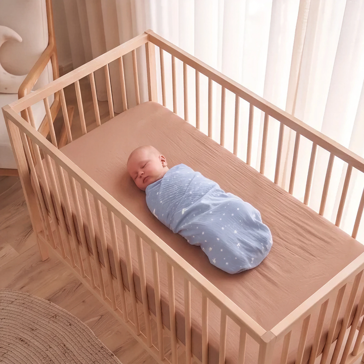Cocoa fitted baby cot sheet on oak cot with swaddled baby, birds eye view - Honey & Sage