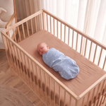 Cocoa fitted baby cot sheet on oak cot with swaddled baby, birds eye view - Honey & Sage