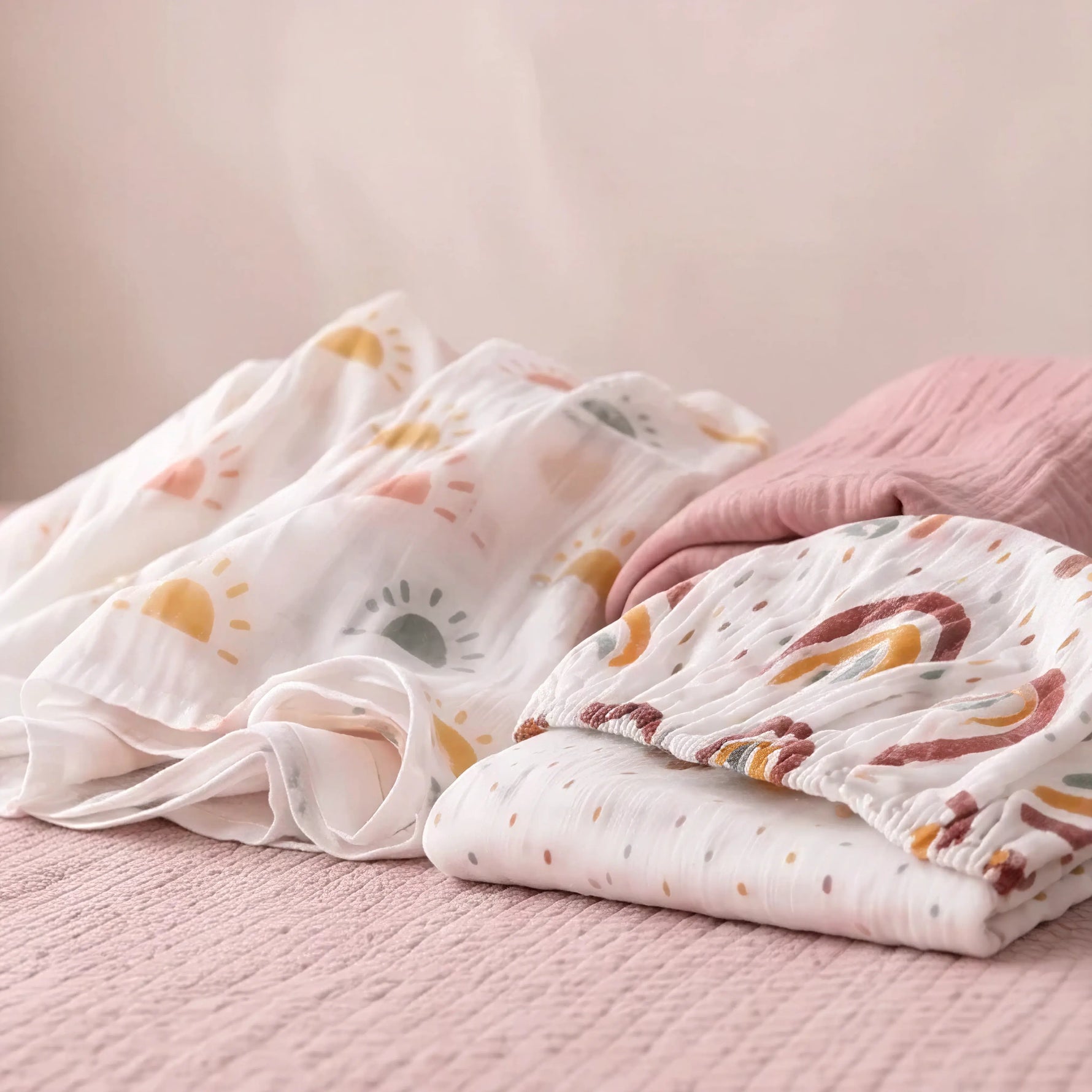 Peony Haze muslin swaddle and Sunbeam fitted cot sheet flat lay with minimalist sun print - Honey & Sage