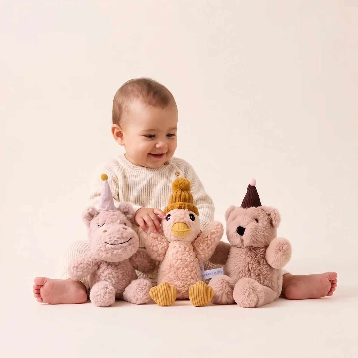 Baby sitting with Coco, Jemima and Arthur plush toys in party hats