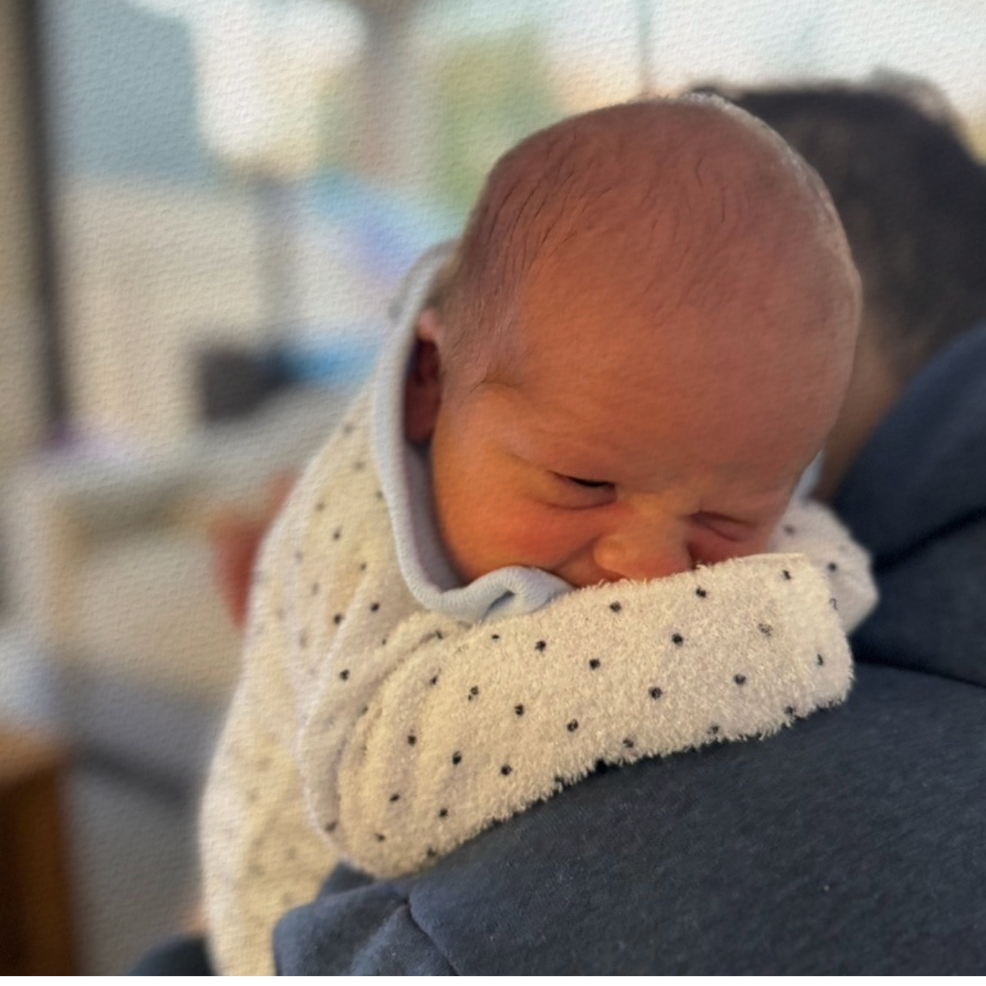 Baby wrapped in a polka dot blanket being held by an adult