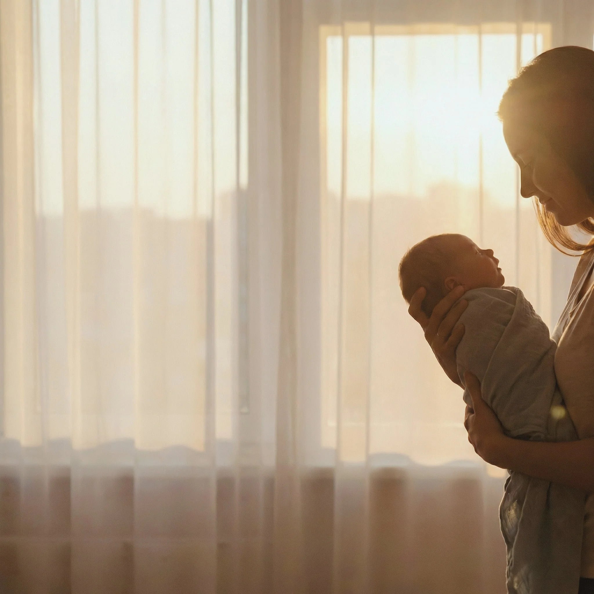 Woman holding a baby in front of sheer curtains with soft lighting