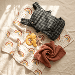 Flatlay showing storm grey baby carrier, baby swaddle, baby teether and patterned cot sheet